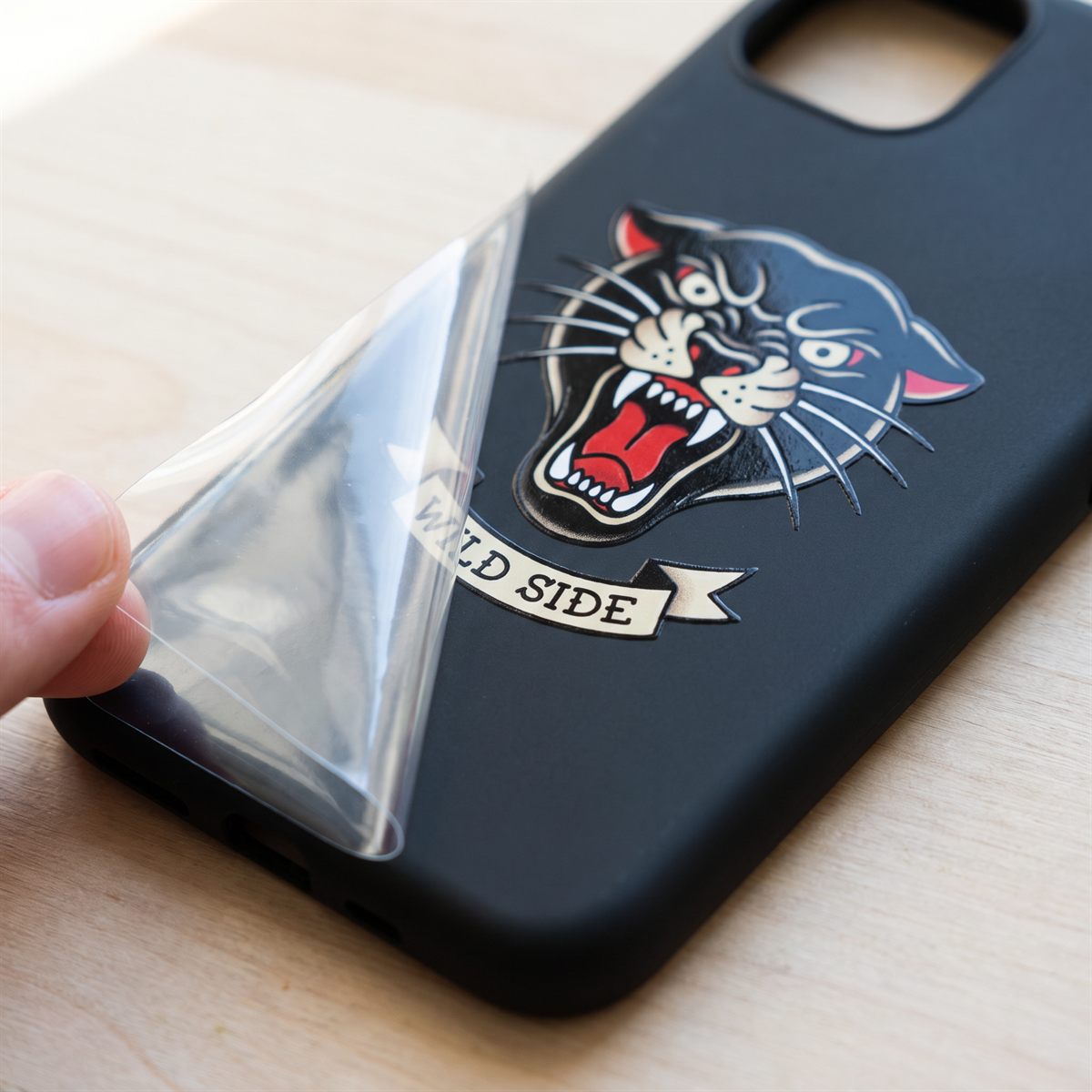 Schwarze Handyhülle, von der die leere Trägerfolie abgezogen wird, Panther-Motiv bleibt auf der Hülle