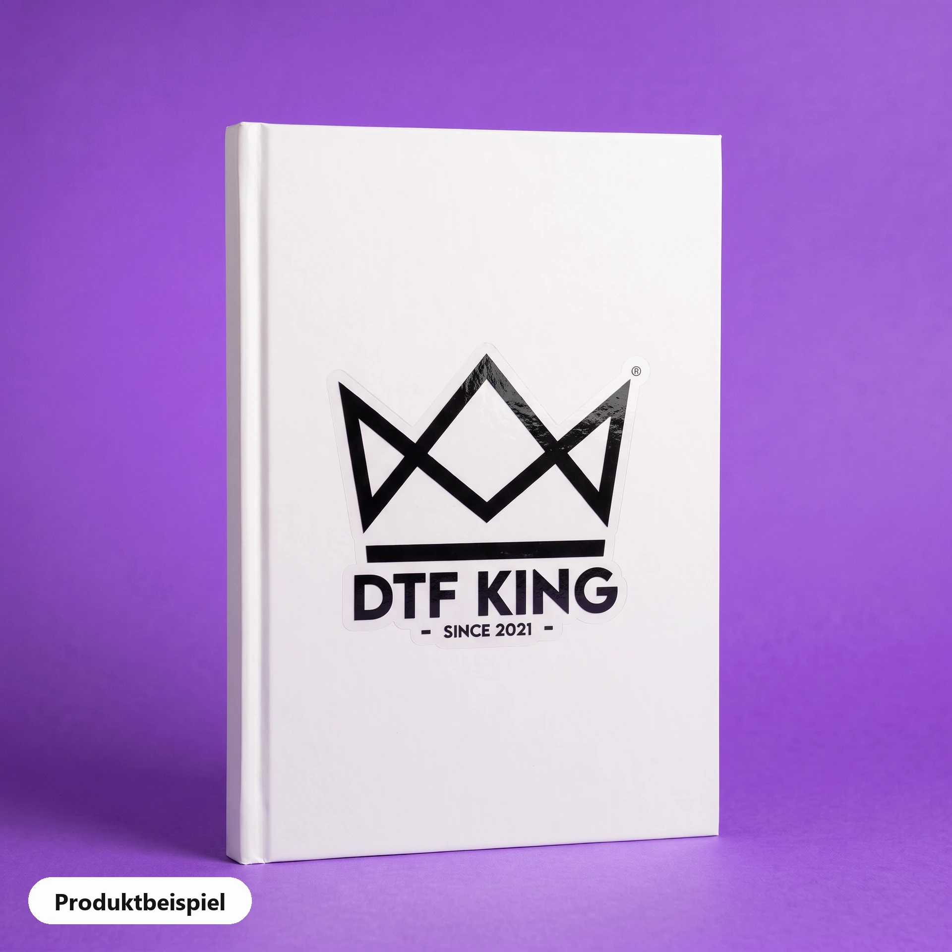 Konturgeschnittener Vinyl-Sticker auf transparenter Folie, glänzend laminiert, mit dem DTF-KING-Logo auf einem Notizbuch