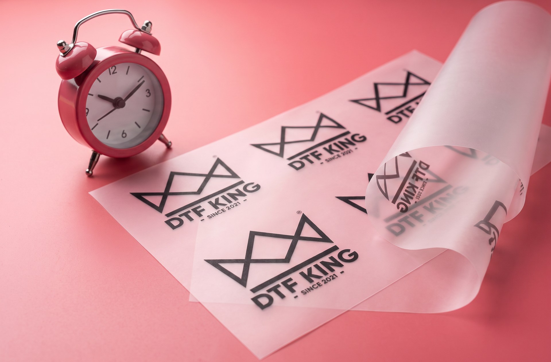 Printed DTF transfer film with DTF-King logos and a pink alarm clock for express production