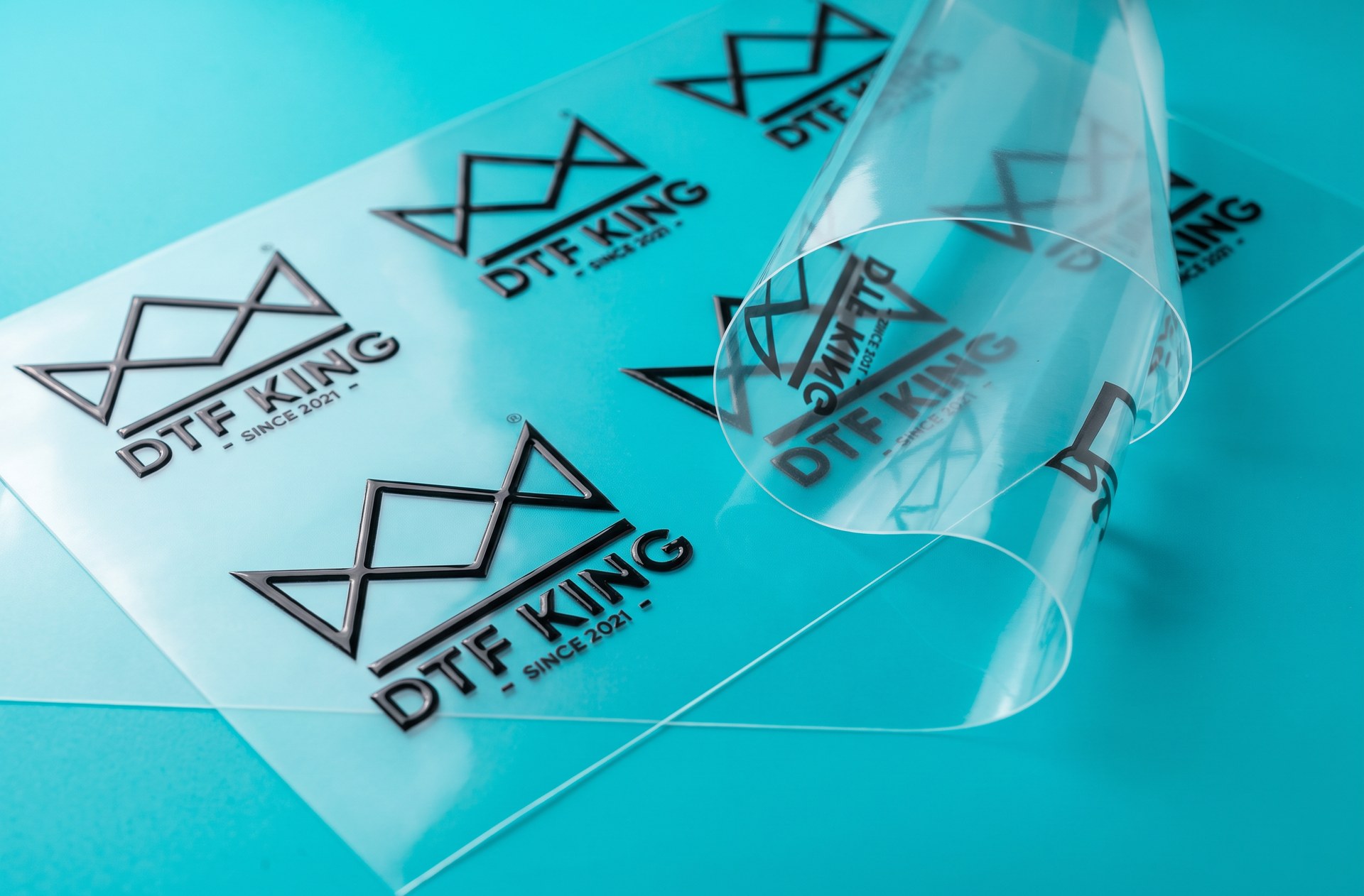 Clear UV DTF transfer film with glossy black printed DTF-King logos on a turquoise background
