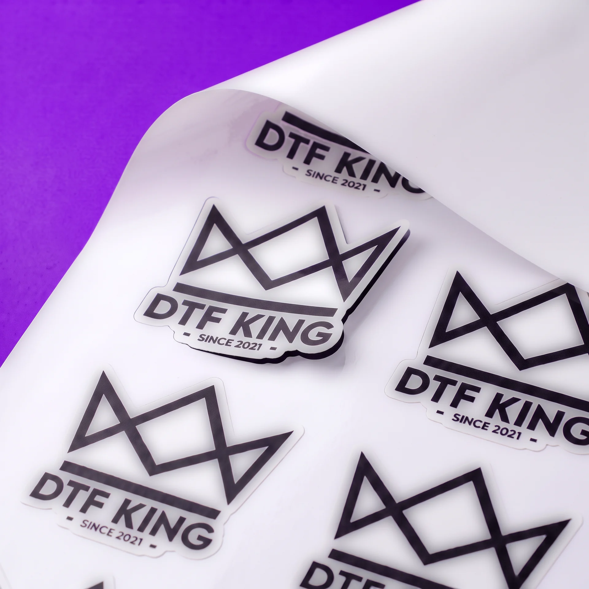 Konturgeschnittene DTF-KING-Vinyl-Sticker auf weißer Trägerfolie, matt laminiert, die Folie ist an einer Ecke hochgeklappt