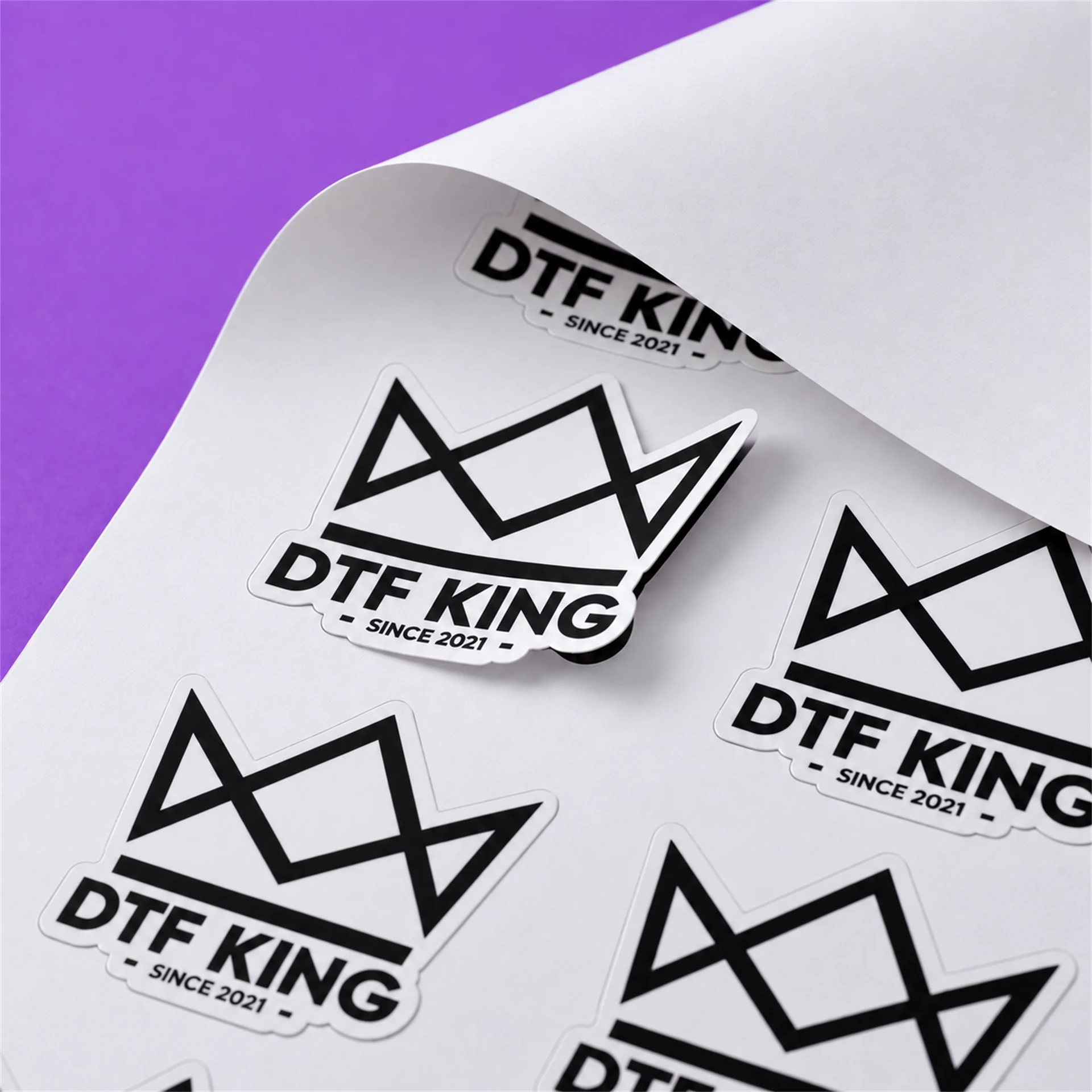 Konturgeschnittene Vinyl-Sticker mit DTF-KING-Logo auf weißer Trägerfolie, matt laminiert, ein Sticker liegt lose auf der Bahn