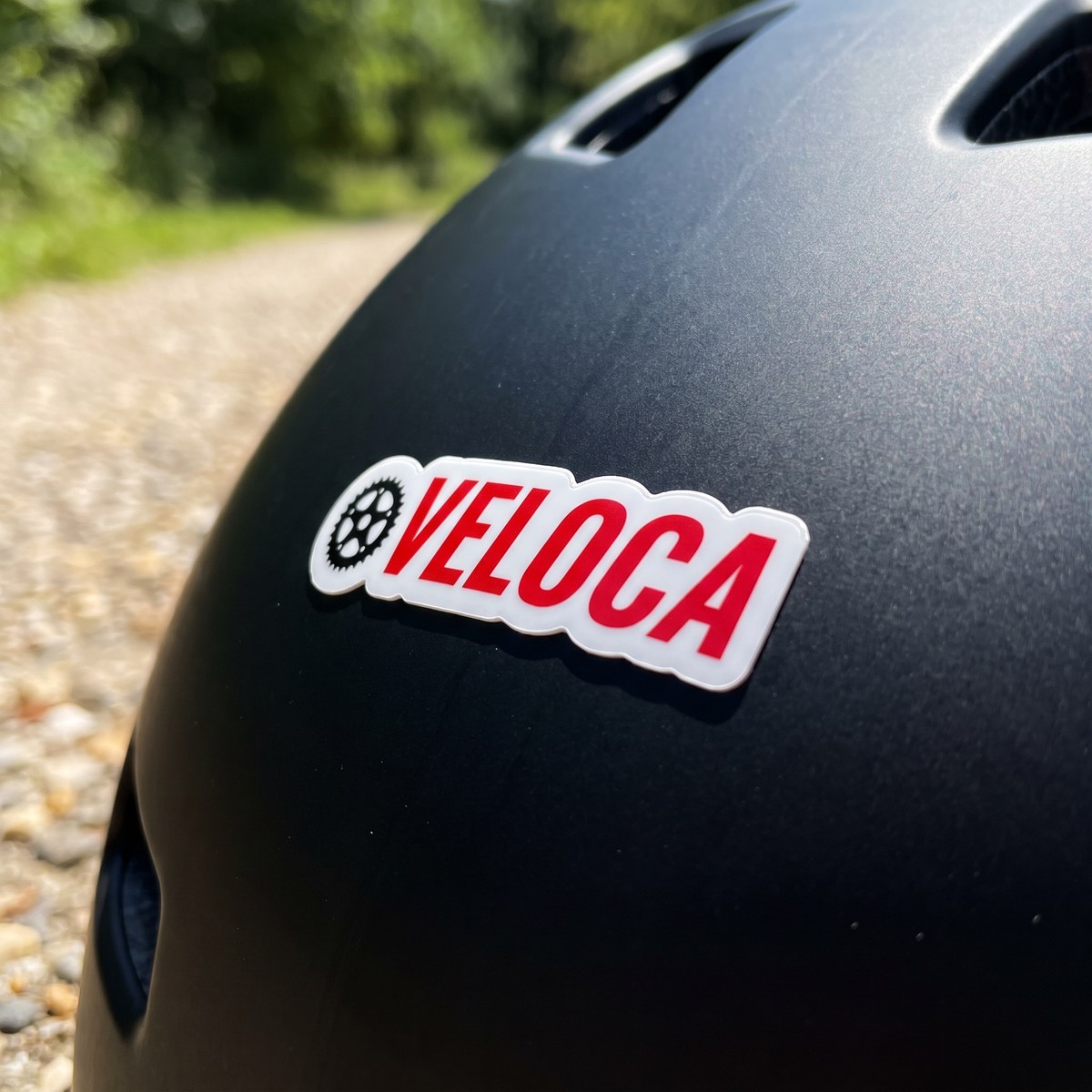 Konturgeschnittener Vinyl-Sticker auf weißer Folie mit dem Logo einer Beispielfirma auf einem matt schwarzen Fahrradhelm