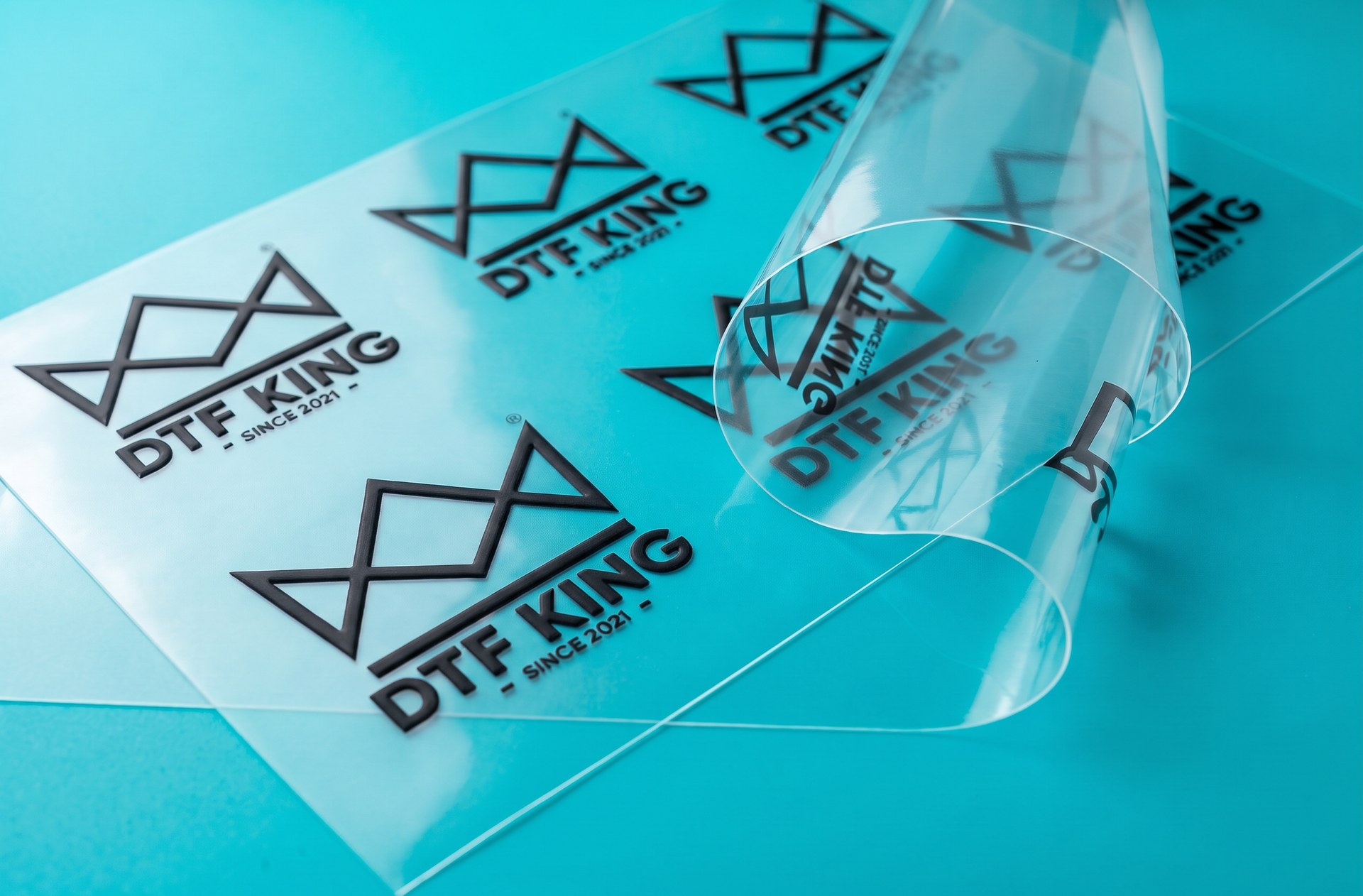 Clear matt UV DTF transfer film with matt black printed DTF-King logos on a turquoise background